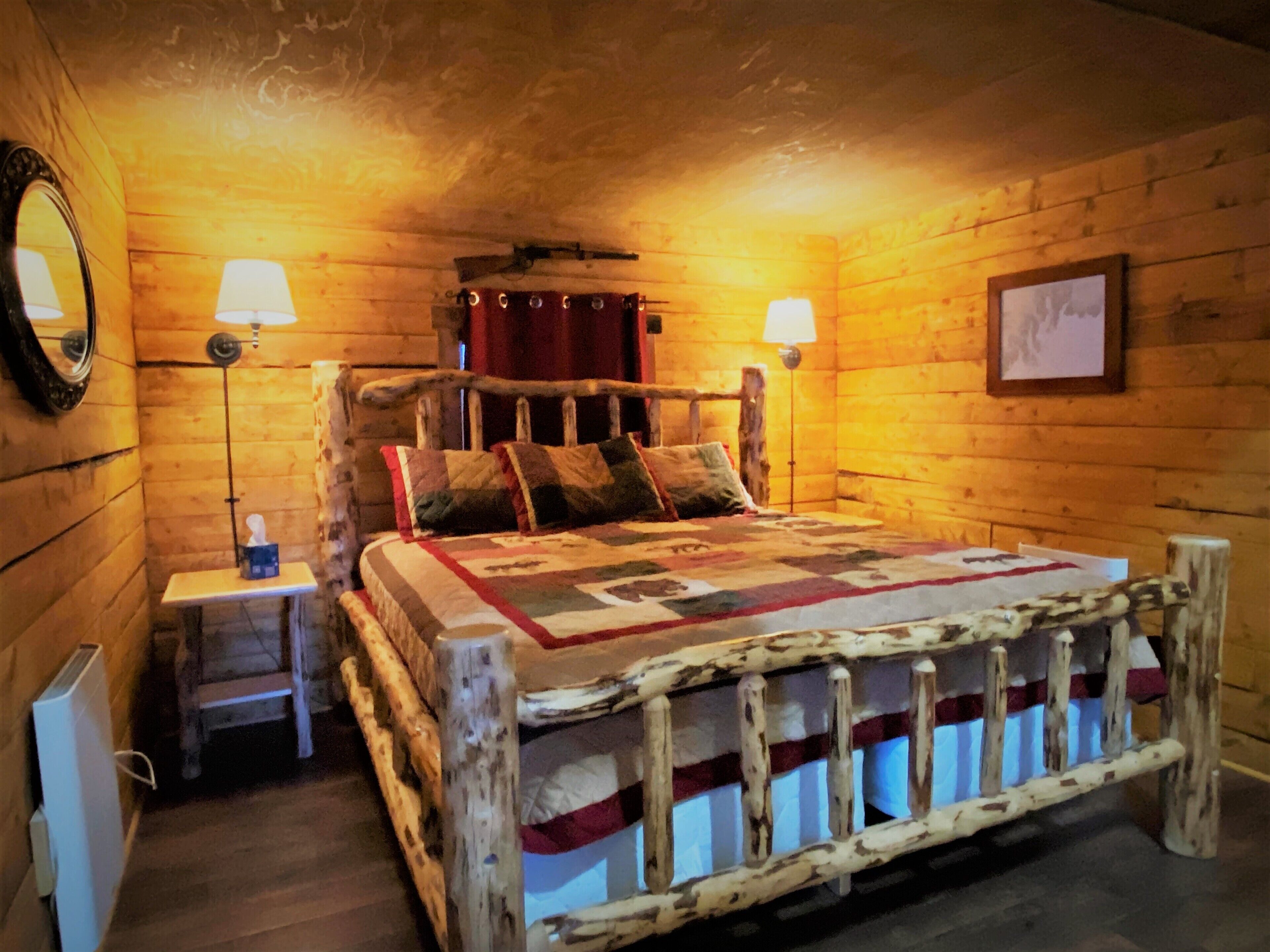 Une chambre à coucher rustique en bois, avec un lit, deux lampes de chevet, un miroir et un tableau encadré au mur.