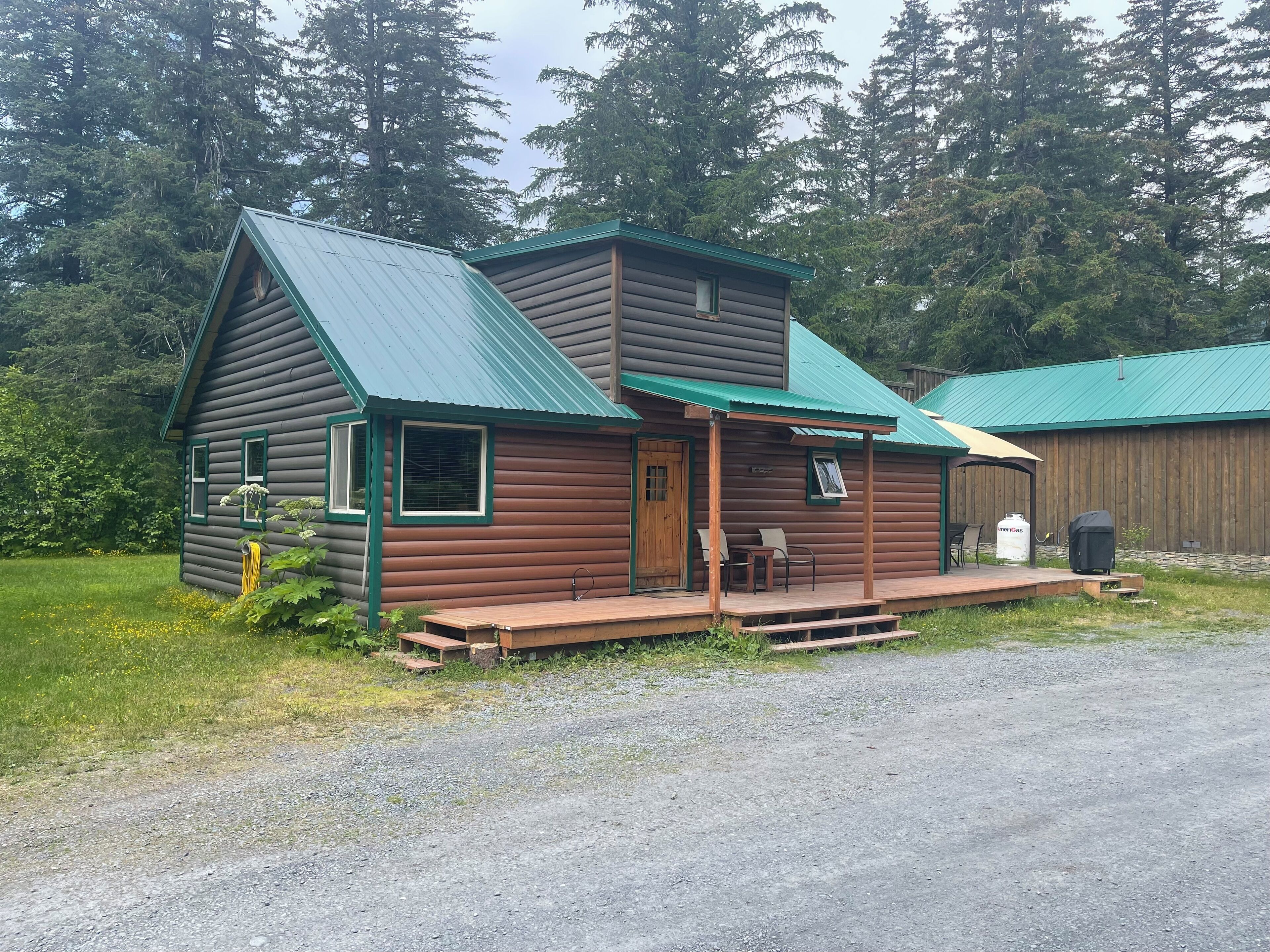 A log cabin with a green roof, a porch with two chairs, and a wooden deck.