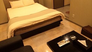 A hotel room with a bed, a black coffee table with a remote control, and a small table with a glass and a tissue box. - My Dear - Adults Only (Osaka)