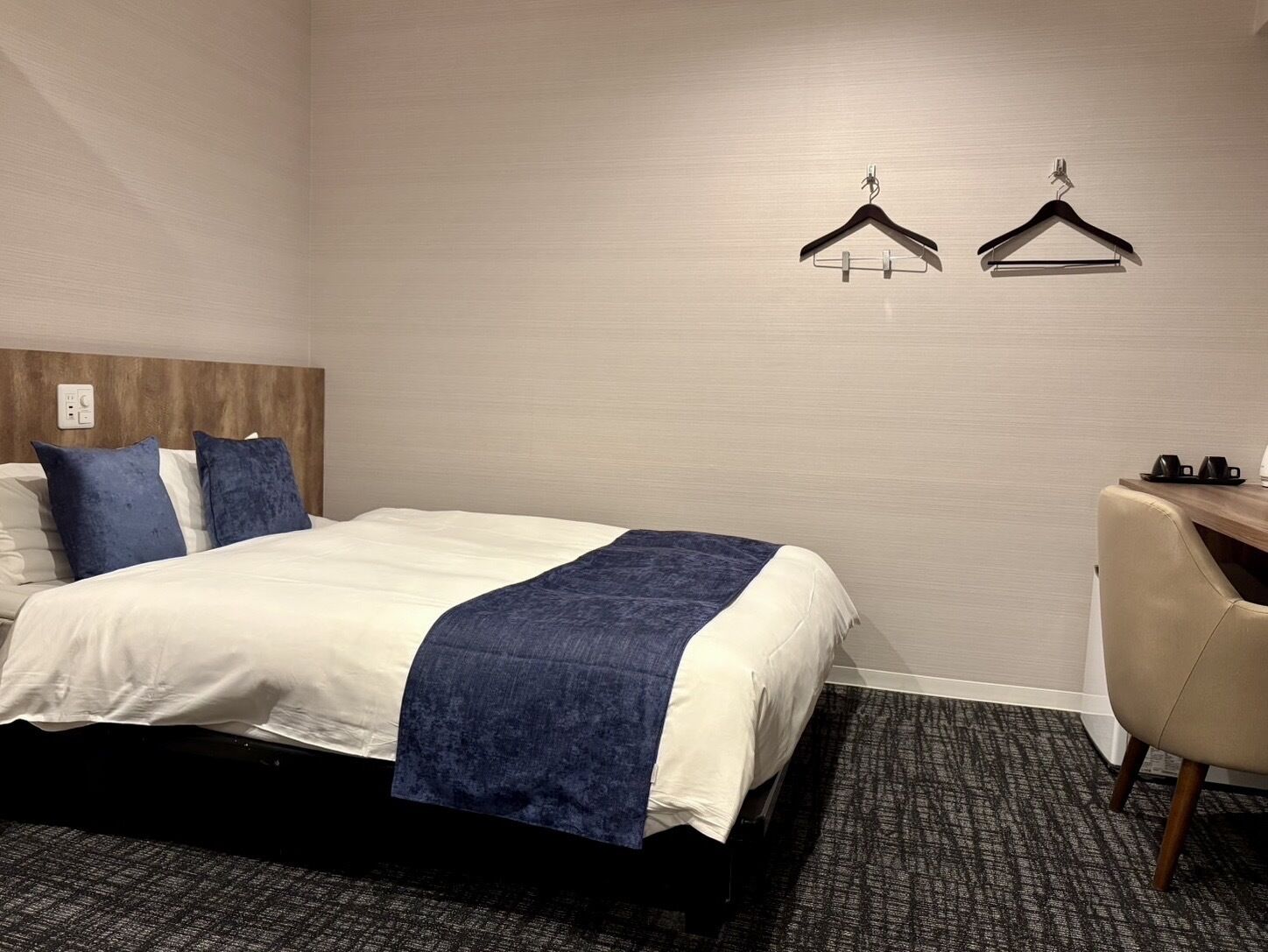 A hotel room with a bed, a desk, and two wall-mounted coat hooks.