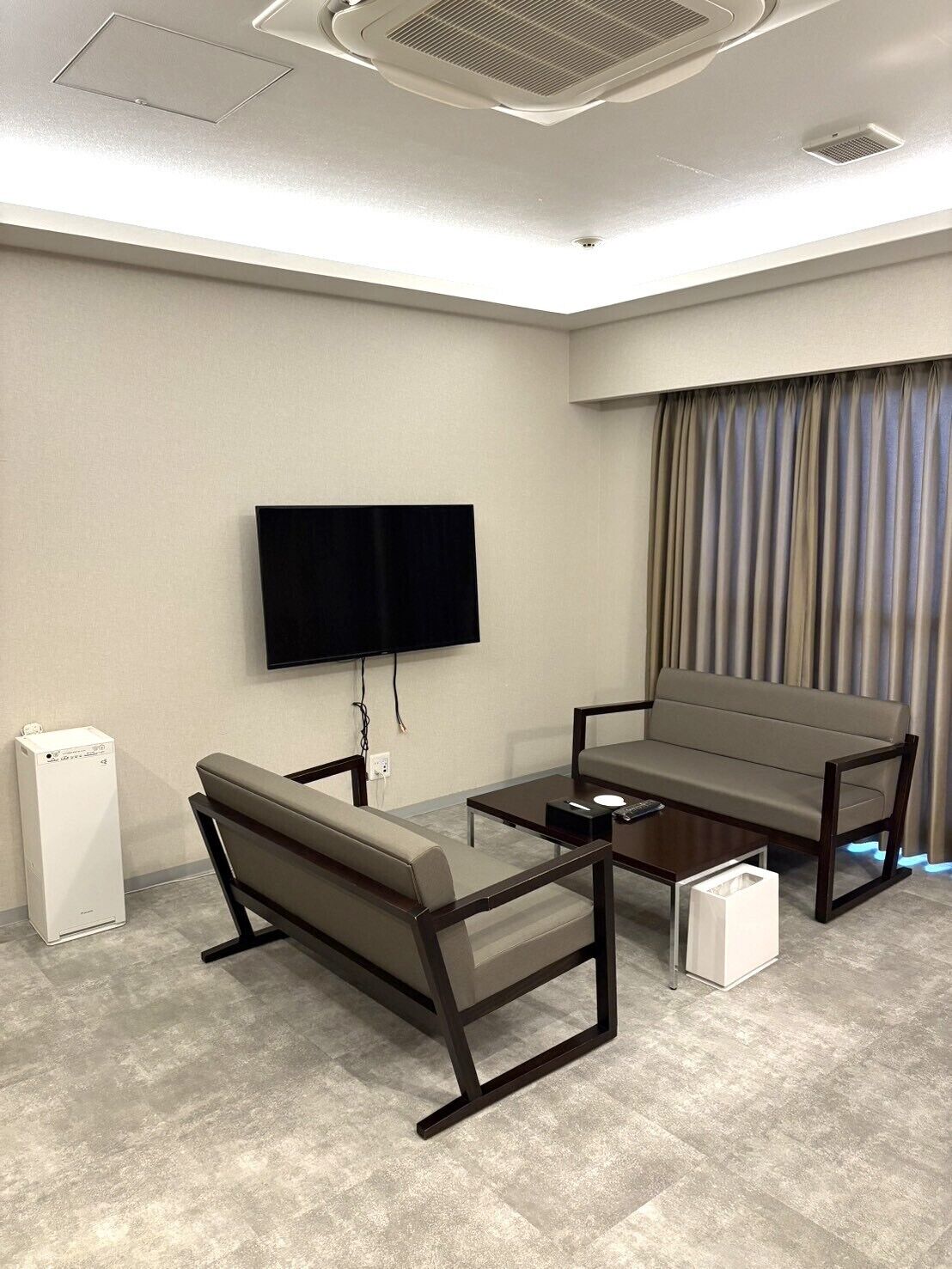 A modern room with a flat-screen TV mounted on the wall, a sofa, a coffee table, and a small white appliance on the floor.