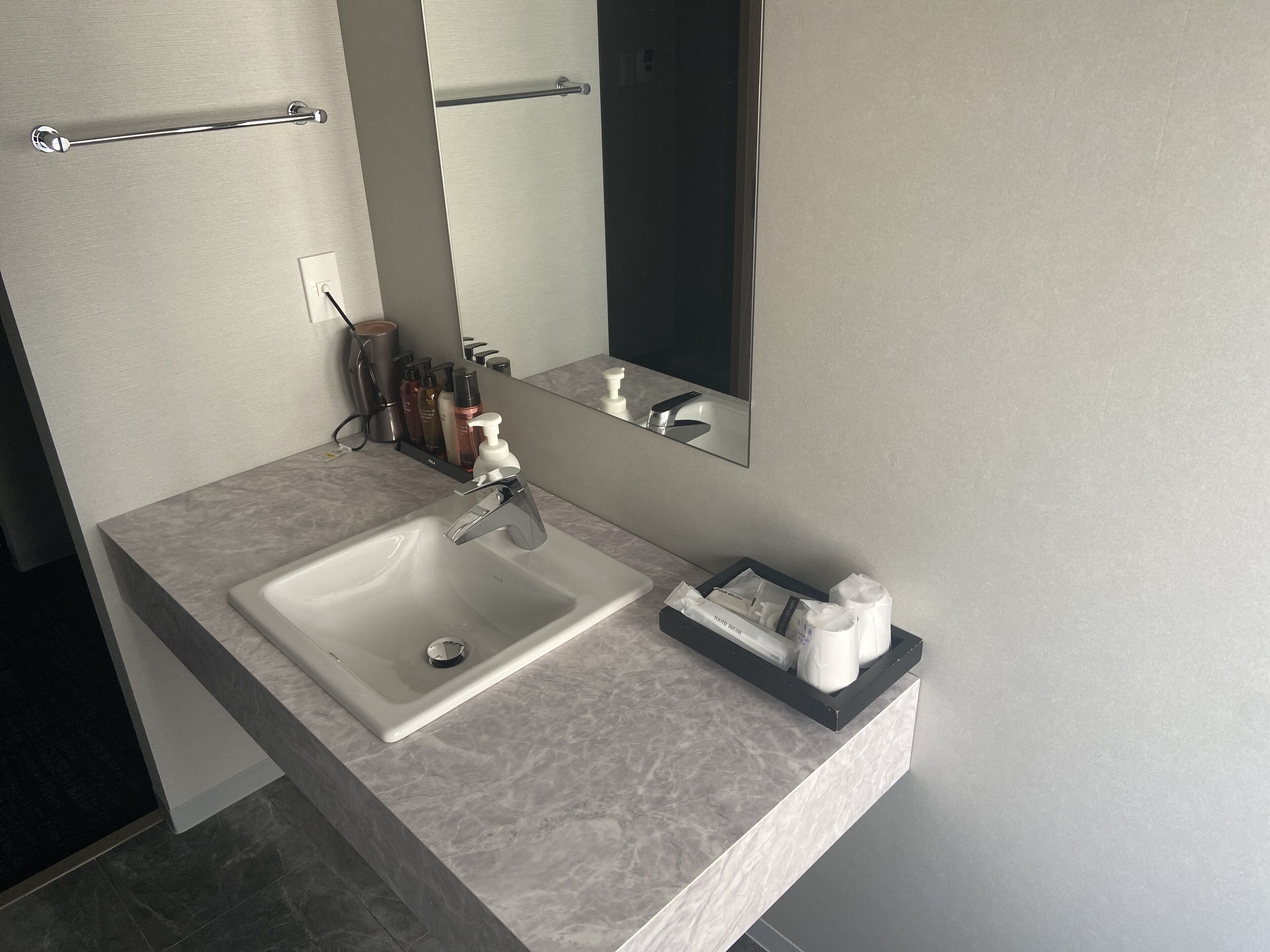 A modern bathroom with a marble sink, a large mirror, and toiletries on the countertop.