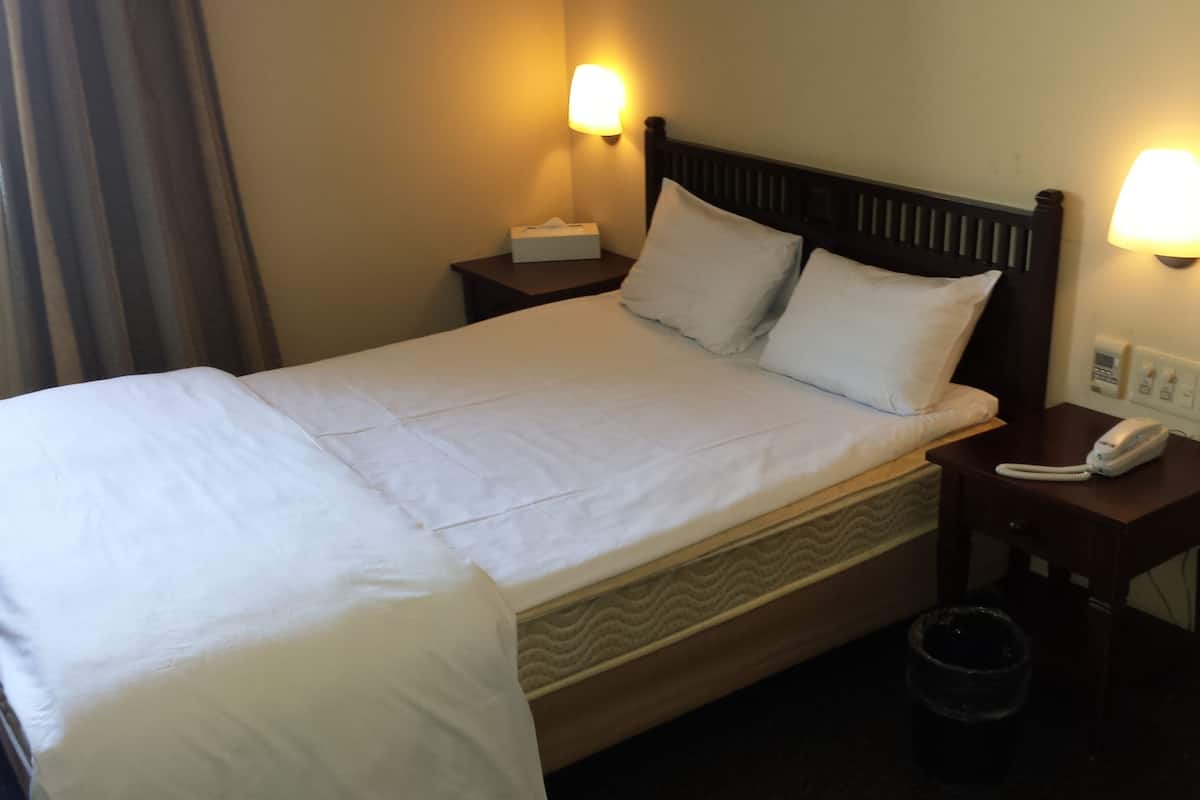 A hotel room with a bed, two bedside lamps, a telephone, and a waste bin.