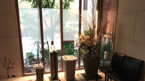 Un área de recepción con un banco, un jarrón grande con flores, un bote de basura y un dispensador de agua.