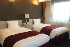 A hotel room with two beds, a nightstand with a lamp, and a window with curtains. - Hotel Monteroza Ohta (Ota)