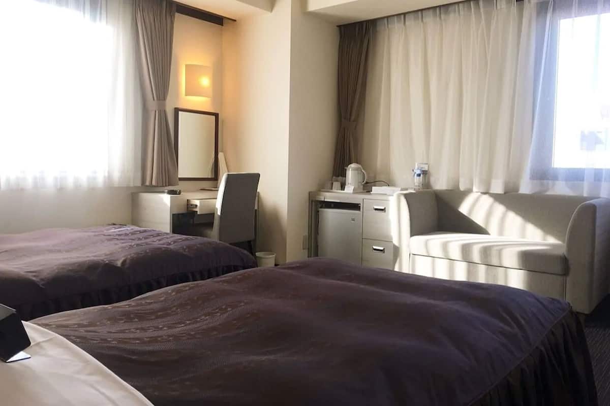 A hotel room with two beds, a desk, a chair, a coffee maker, and a mirror.
