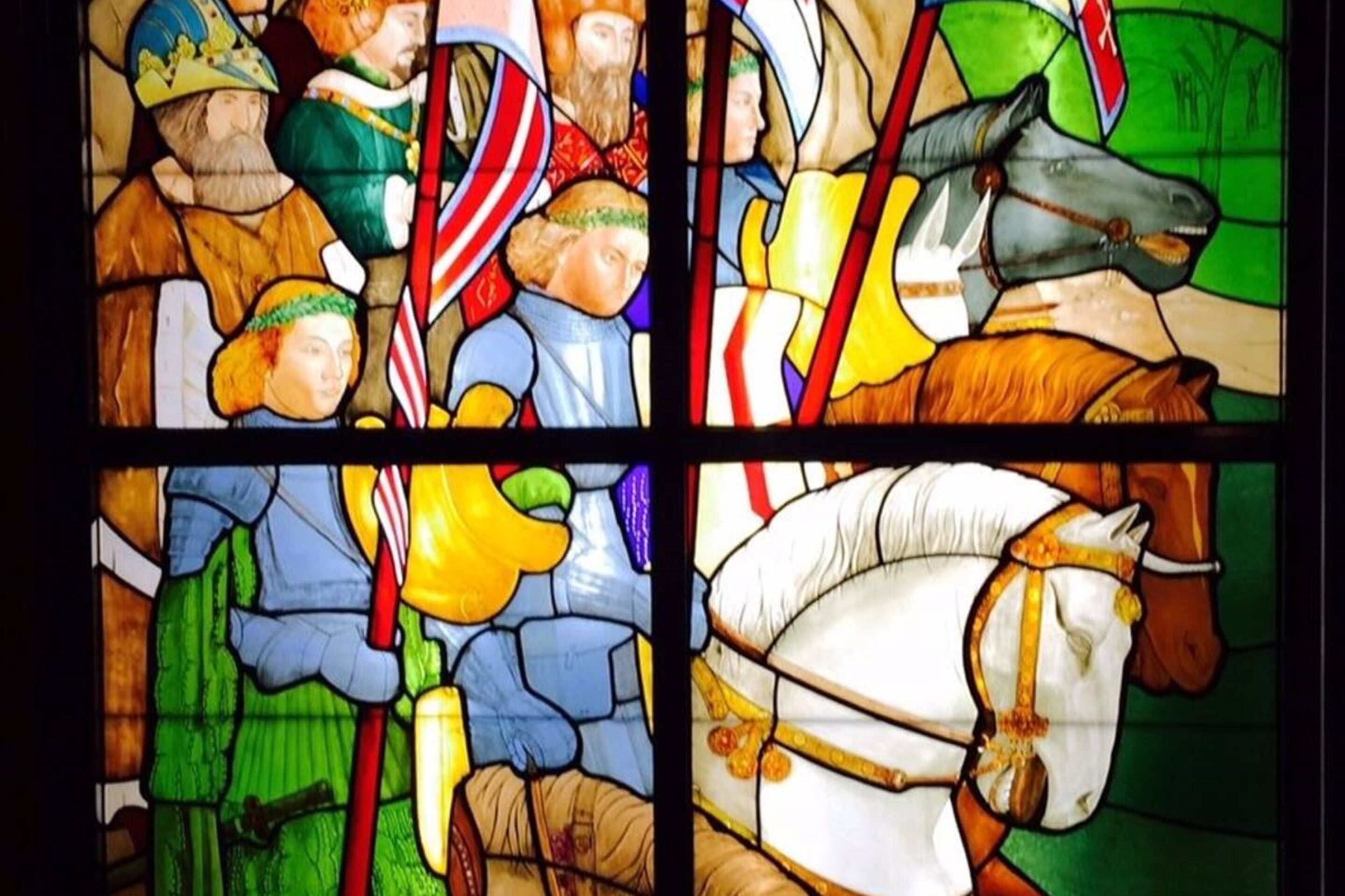 A stained glass window with four panels depicting figures and a horse.