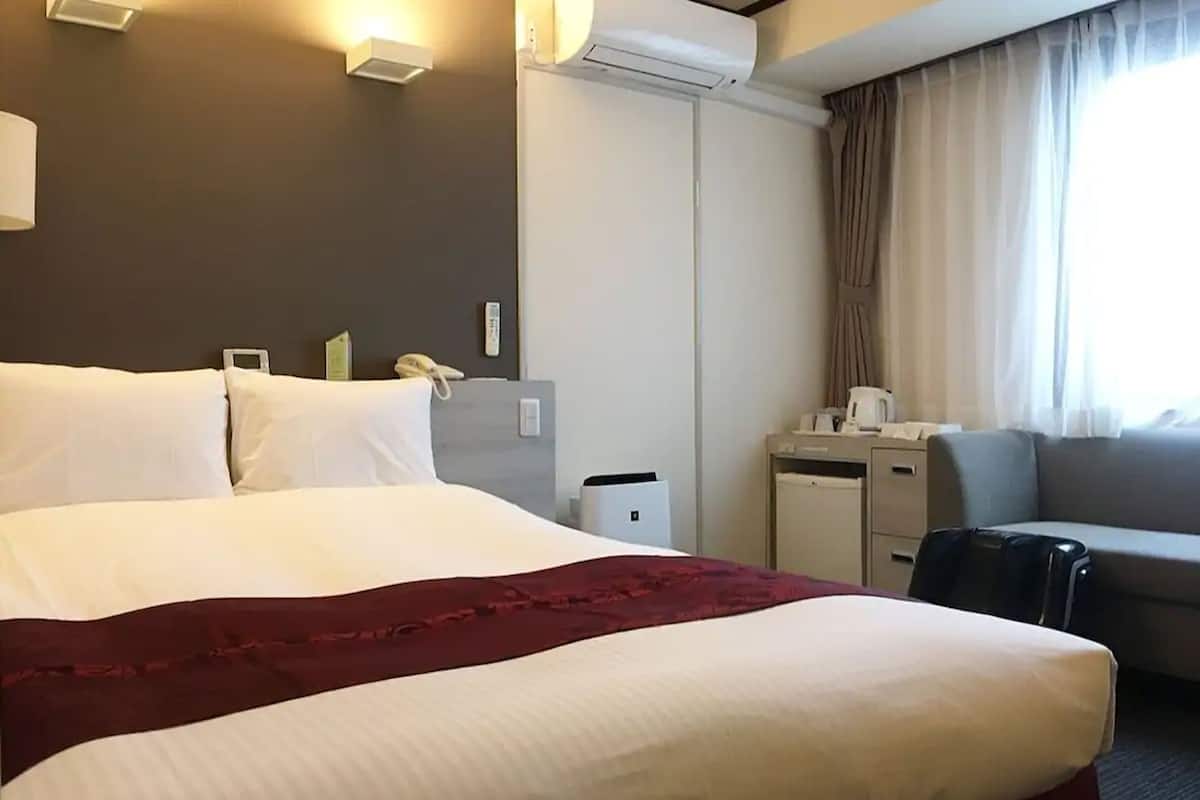 A hotel room with a large bed, a desk, a chair, a sofa, and a window with curtains.