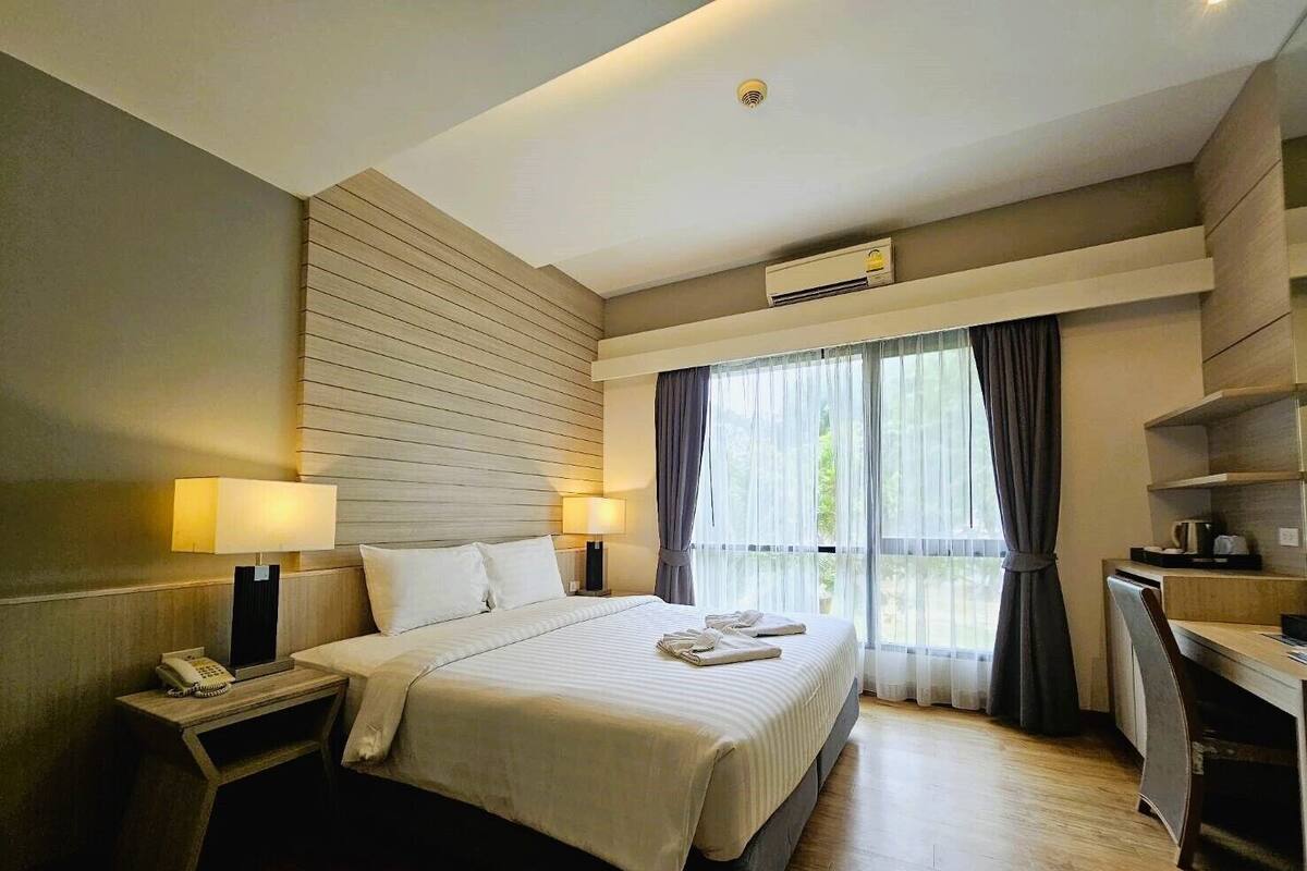A hotel room with a large bed, bedside lamps, a desk, and a window with curtains.