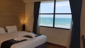 A hotel room with a large bed, a nightstand, a lamp, and a window with a view of the ocean. - Du Talay Hotel Koh Chang (Ko Chang)
