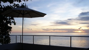 A balcony with a view of the sea at sunset, a table, and an umbrella. - Du Talay Hotel Koh Chang (Ko Chang)