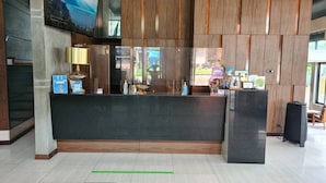 A reception desk with a dark countertop, wooden paneling on the walls, and a large window providing a view of the outdoors. - Du Talay Hotel Koh Chang (Ko Chang)