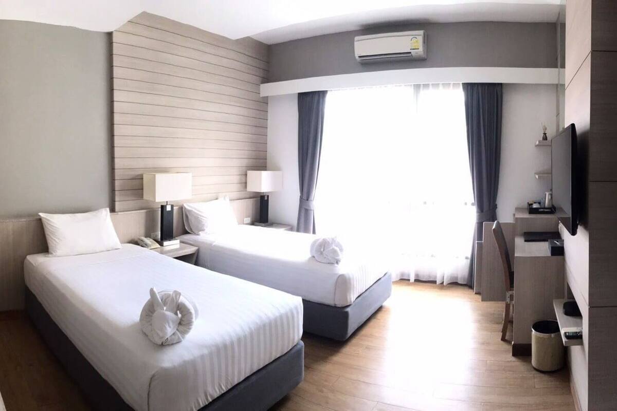 A hotel room with two beds, a desk, a TV, and a window with curtains.
