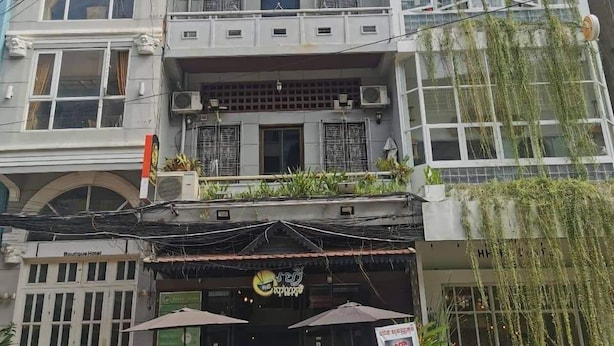 A multi-story building with balconies, a storefront with umbrellas, and a sign for a hotel. - Sovanphum Guesthouse (Phnom Penh)