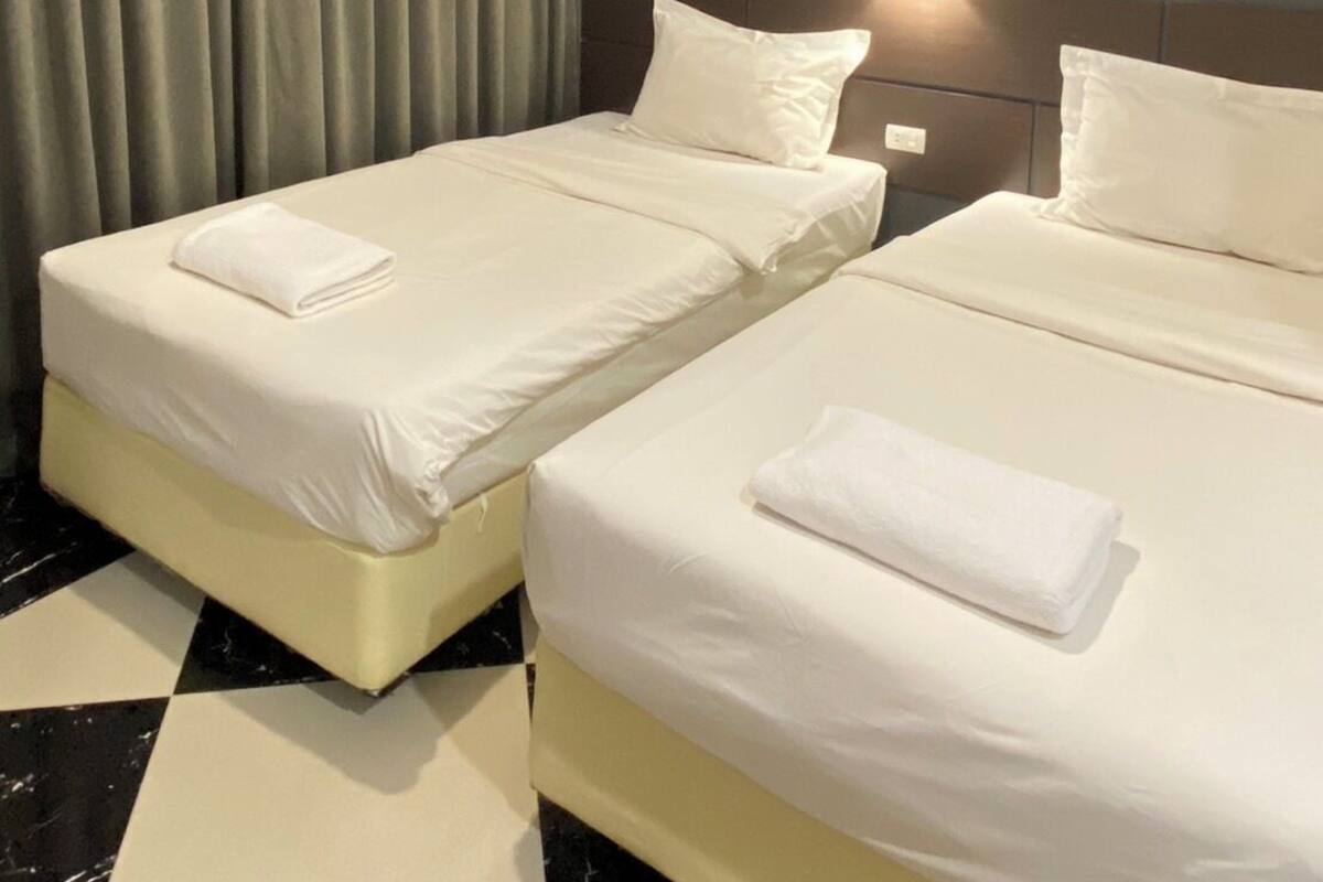 Une chambre d’hôtel avec deux lits, une grande fenêtre avec des rideaux, un lampadaire fixé au mur et un tableau encadré.