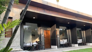 Un bâtiment moderne doté d’un espace extérieur couvert avec des sièges, de grandes fenêtres et d’une pelouse bien entretenue.