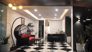 Un intérieur moderne avec un sol à carreaux, un fauteuil suspendu en forme de sphère, un piano et un comptoir d’accueil.