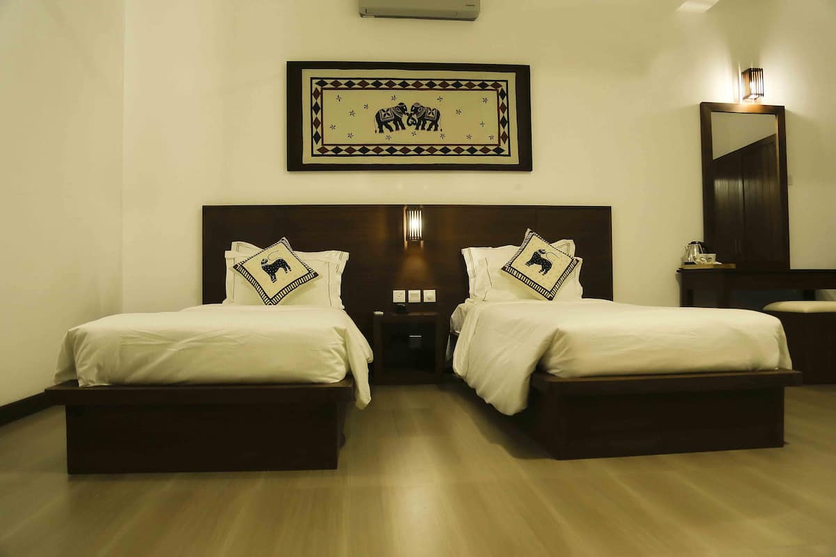Habitación de hotel con dos camas individuales, una mesita de noche, un cuadro enmarcado sobre las camas, un espejo y una lámpara de noche.
