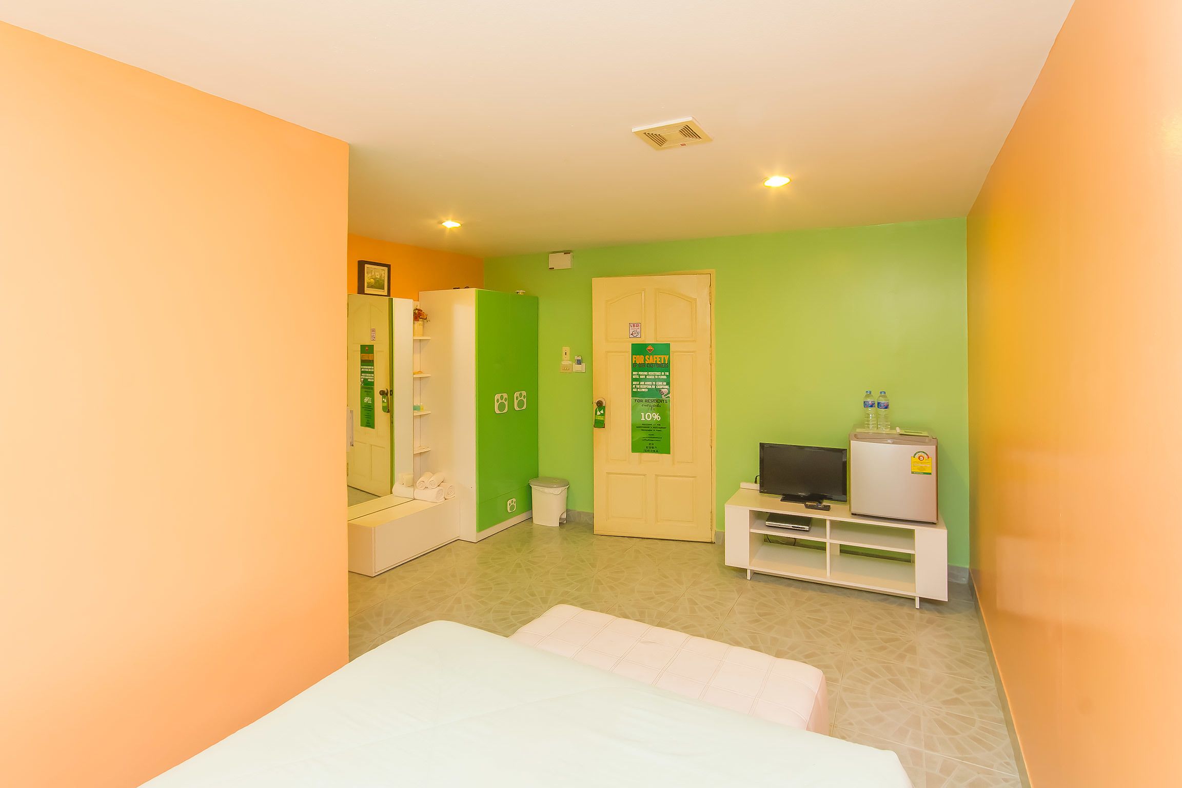 A hotel room with a bed, a television, a mini-fridge, and a door with a safety sign.