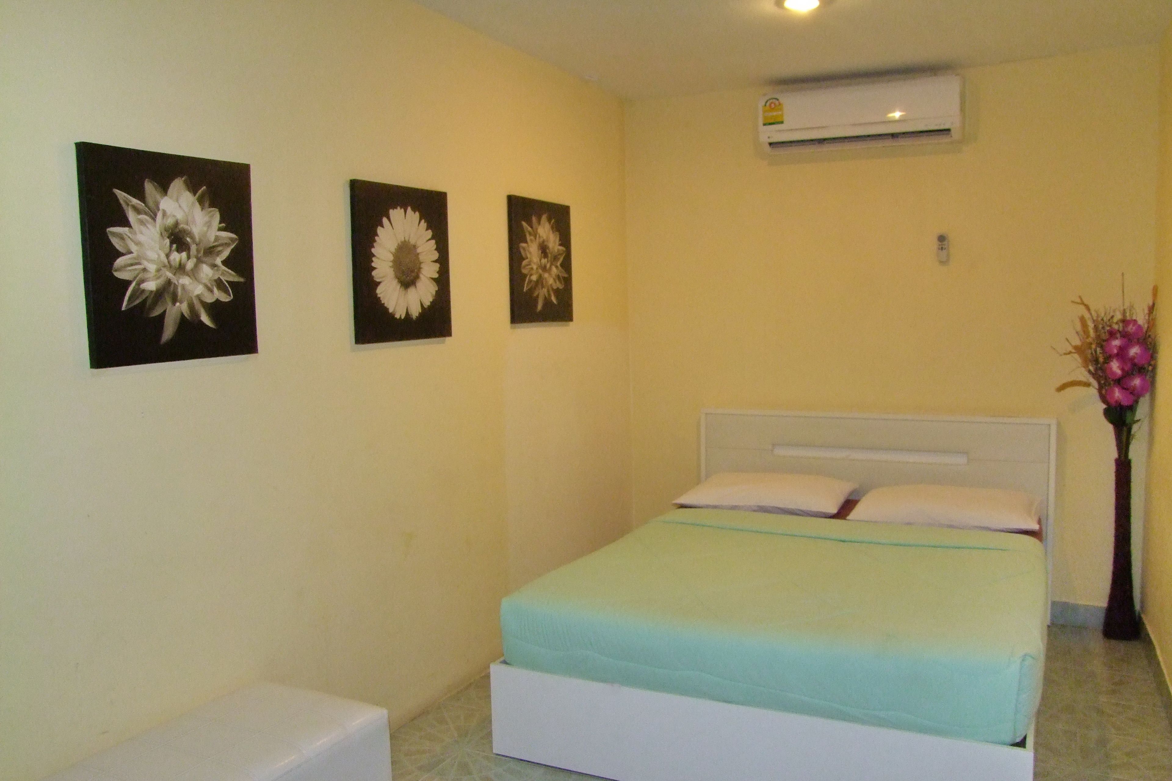 Une chambre à coucher comprenant un lit, une table de chevet et trois tableaux représentant des fleurs, accrochés au mur.