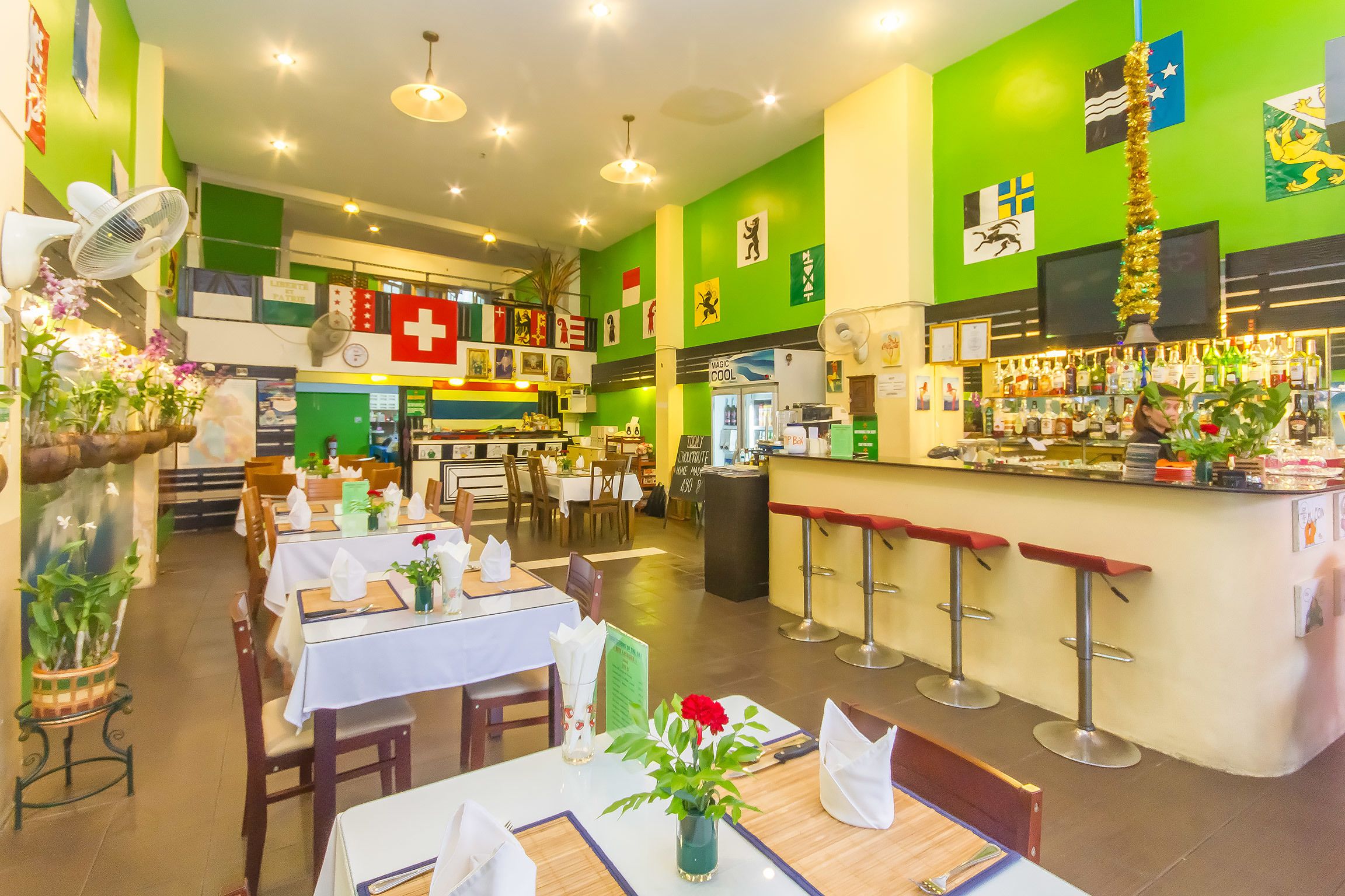 A restaurant with multiple dining tables, a bar area, and various flags on the walls.