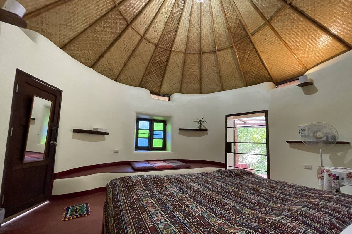 A bedroom with a large bed, a small window, a door, and a ceiling fan.
