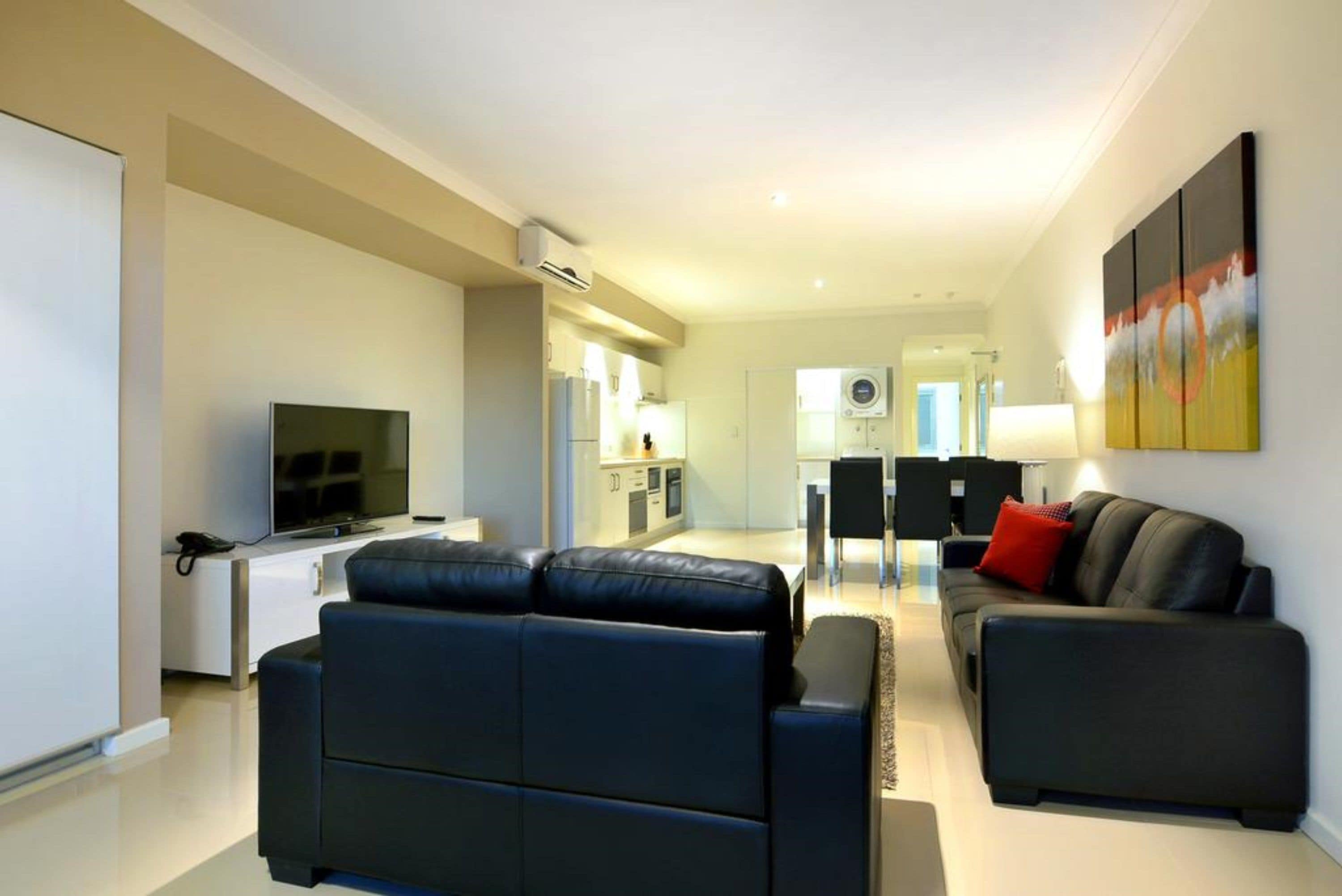 Una sala de estar moderna con un sofá, una televisión y un comedor con mesa y sillas.