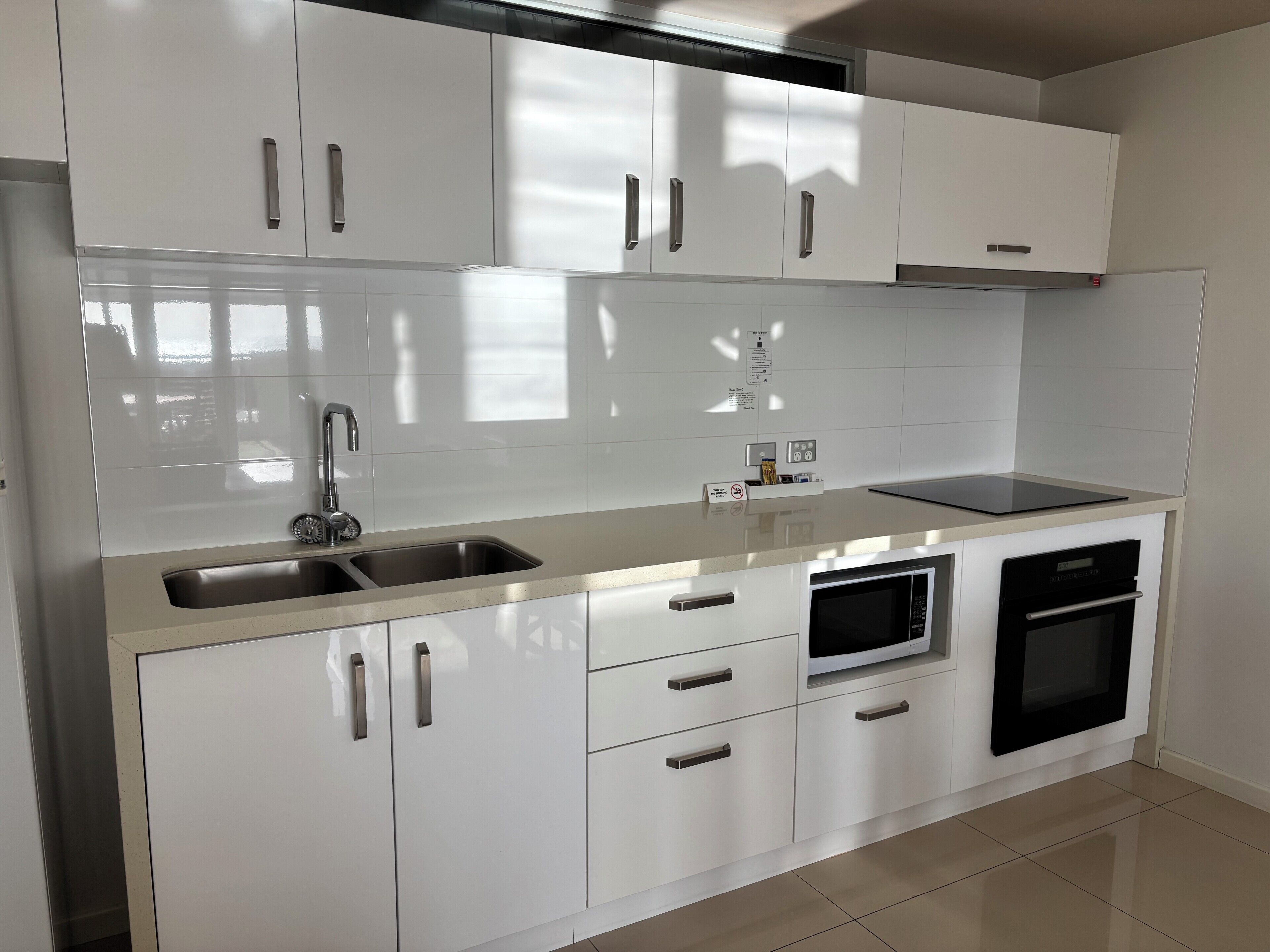 Una cocina moderna con armarios blancos, un lavamanos de acero inoxidable y un horno empotrado.