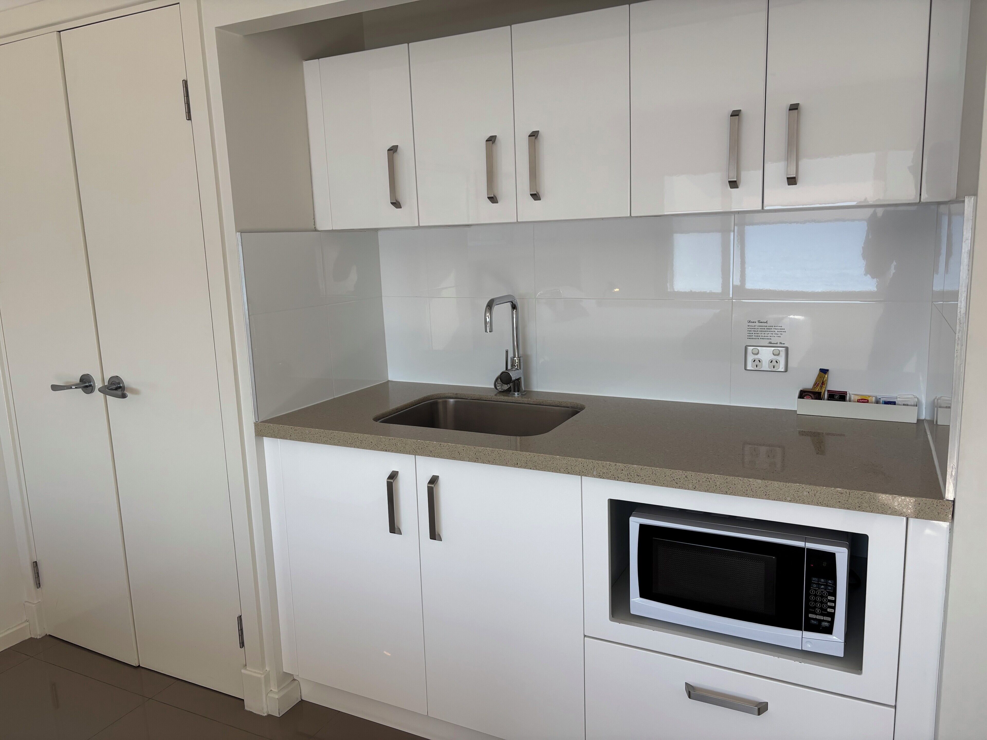A kitchen with white cabinets, a stainless steel sink, and a built-in microwave.