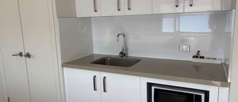 Una cocina con gabinetes blancos, un lavamanos de acero inoxidable y un microondas integrado.