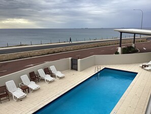 Une piscine avec des chaises longues, une vue sur la mer et une route où l’on peut marcher.