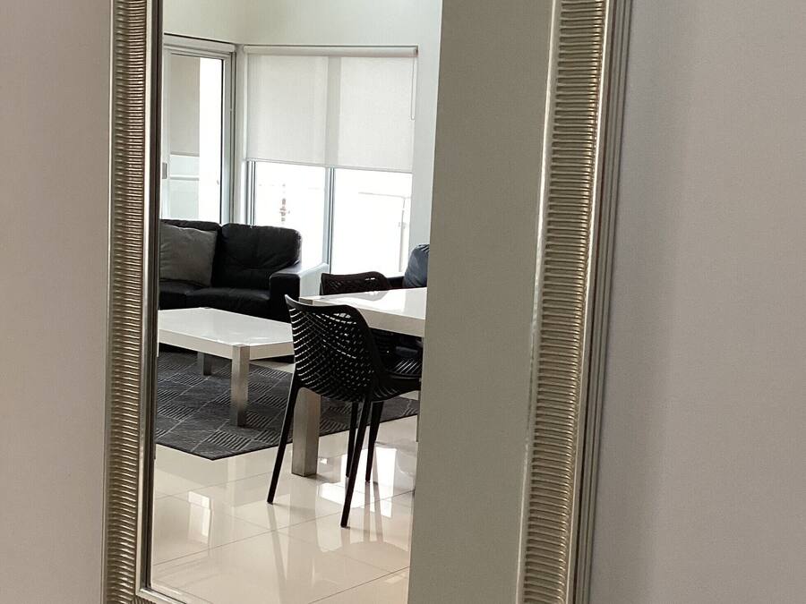 Een spiegel met een ribbelig frame dat een moderne woonkamer weerspiegelt, met een bank, een tafel en stoelen.