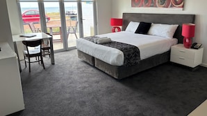 Une chambre d’hôtel moderne avec un grand lit, un bureau et une vue sur l’extérieur, accessible par une porte-fenêtre coulissante.