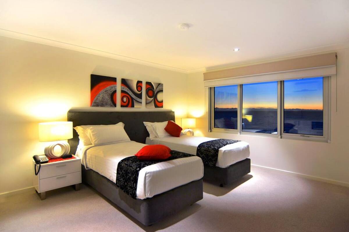 Een moderne hotelkamer met twee bedden, een groot raam met uitzicht op de stad, en een schilderij boven het bed.