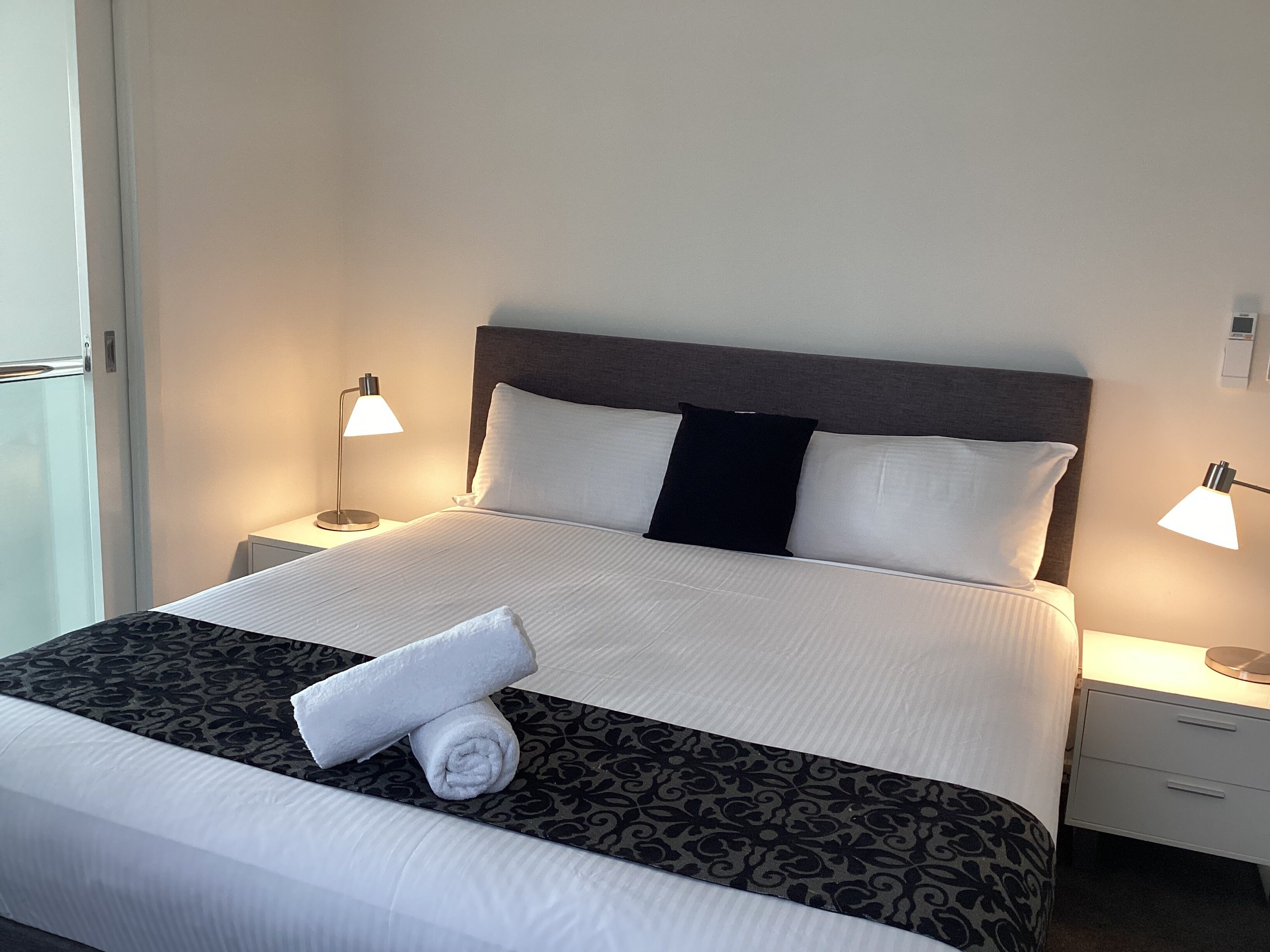 Una cama bien hecha con ropa de cama blanca y negra, dos lámparas de noche y una mesita de noche blanca.
