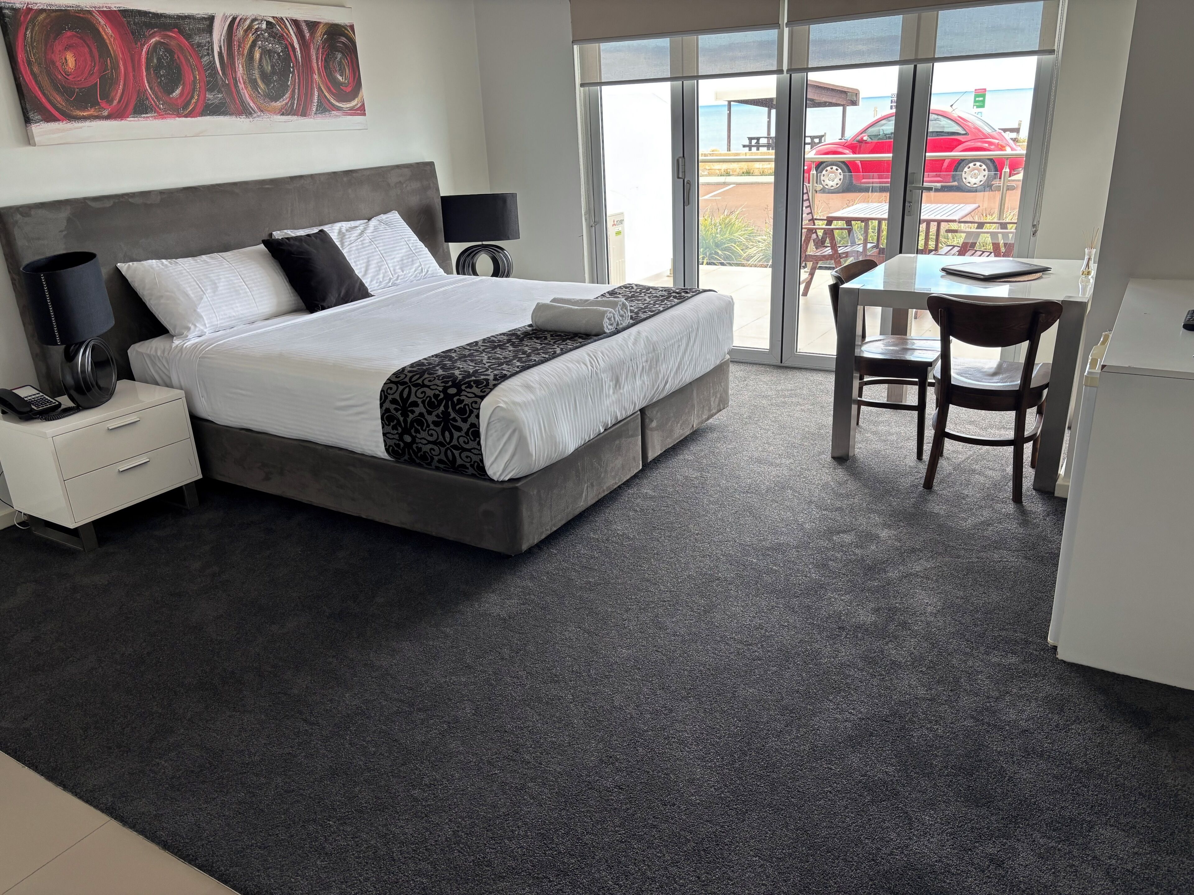 A modern hotel room with a large bed, bedside lamps, a desk, and a view of the outside.