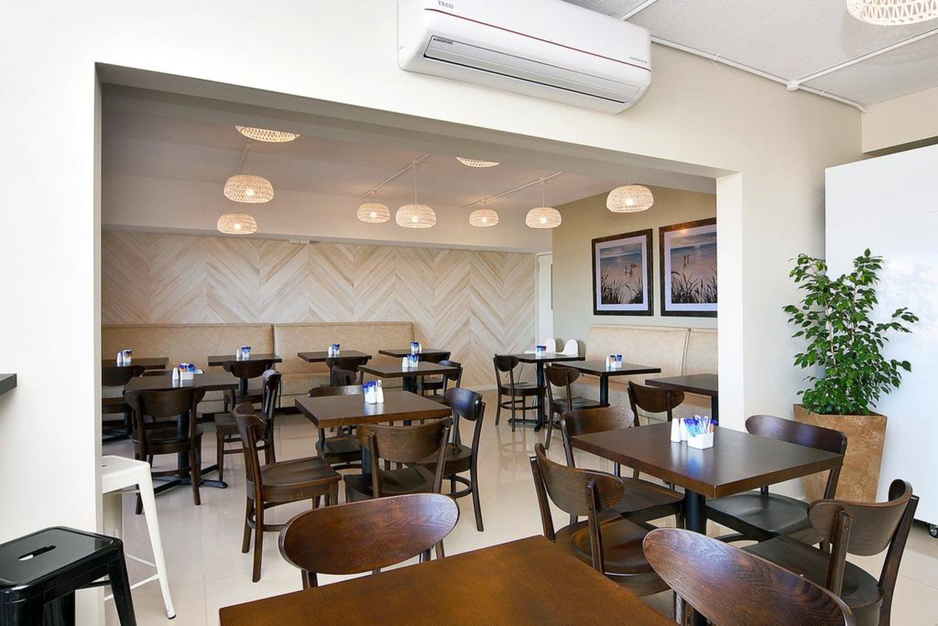 A modern restaurant interior with wooden tables and chairs, pendant lighting, and a herringbone-patterned wall.