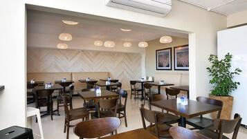 Un interior de restaurante moderno con mesas y sillas de madera, iluminación colgante y una pared con estampado en espiga.