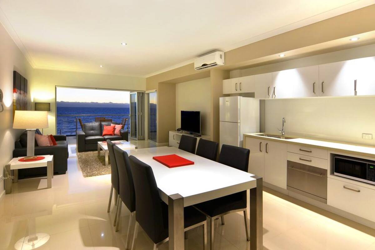 Una cocina moderna con comedor, televisor y vista al mar.
