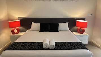 A neatly made bed with a black headboard, two bedside lamps, and a pair of rolled towels on the bed.