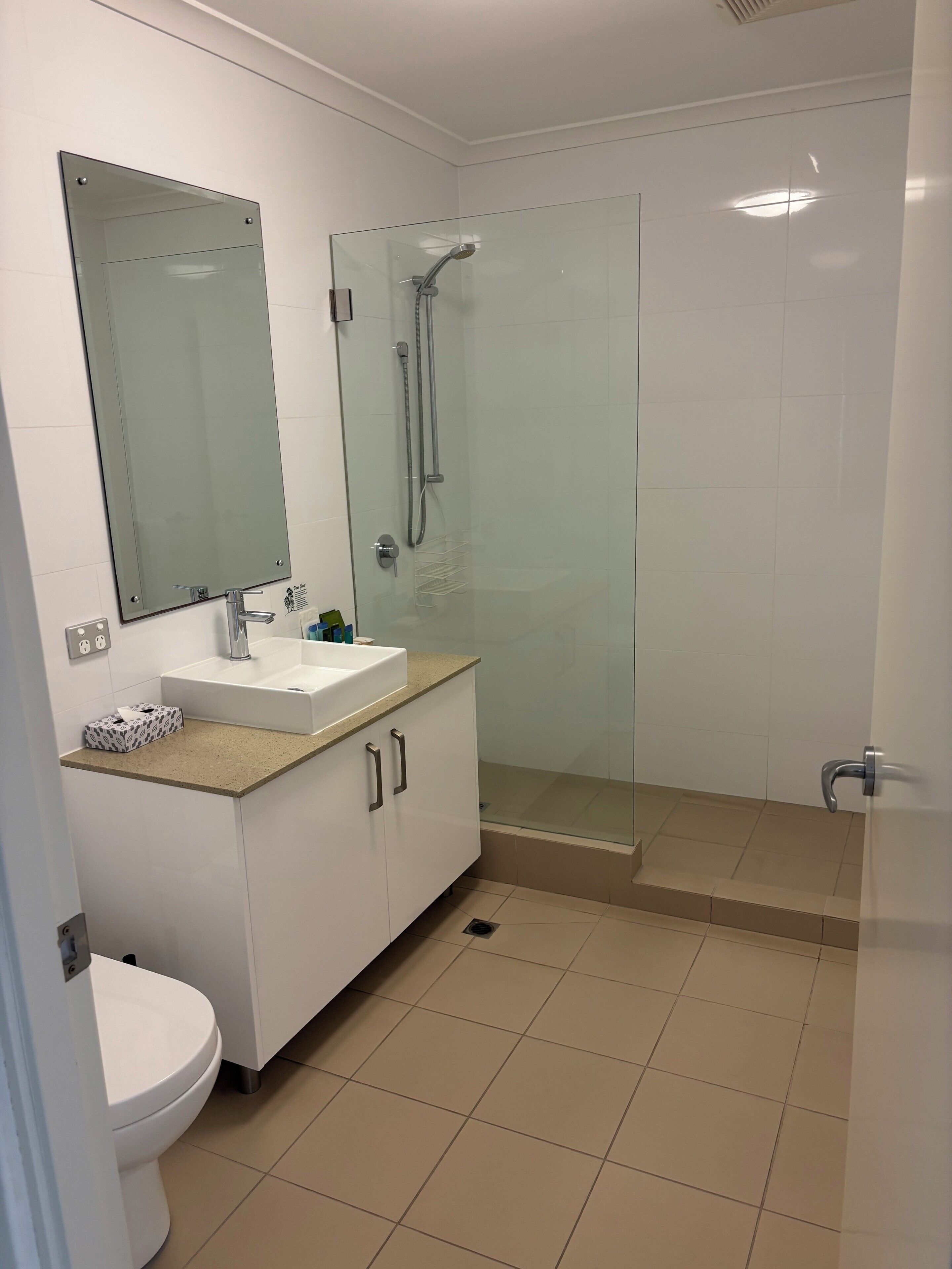 Un baño con inodoro, lavamanos, espejo, ducha y suelo de baldosas.