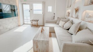 A modern living room with a large TV, a wooden coffee table, and a sofa with cushions. There is a window with a view of the sea. - BeachHouse Geragera (Kobe)