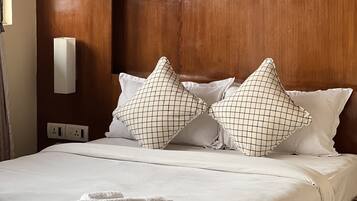 A neatly made bed with white linens, two patterned pillows, and a pair of folded towels.