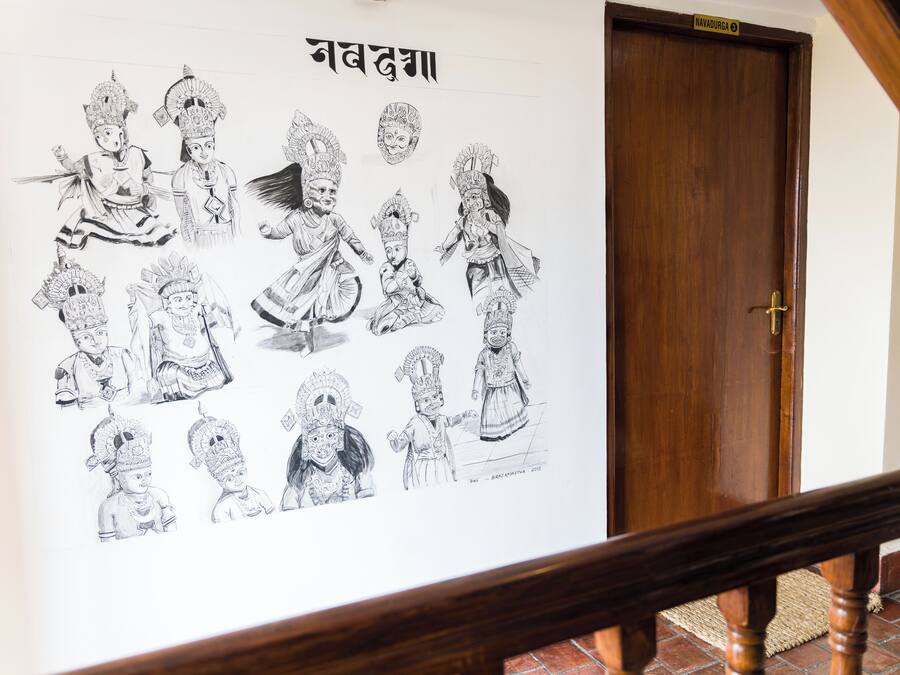 Een muur met zwart-wit schetsen van figuren, een houten deur en een trapleuning.