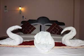 A bed with a headboard, two pillows, and two towels arranged in a swan shape. - Festoon Hotel (Kathmandu)