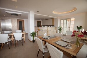 A modern dining area with a wooden table set for four, white chairs, and a potted plant. - Hotel Aysima (Kas)