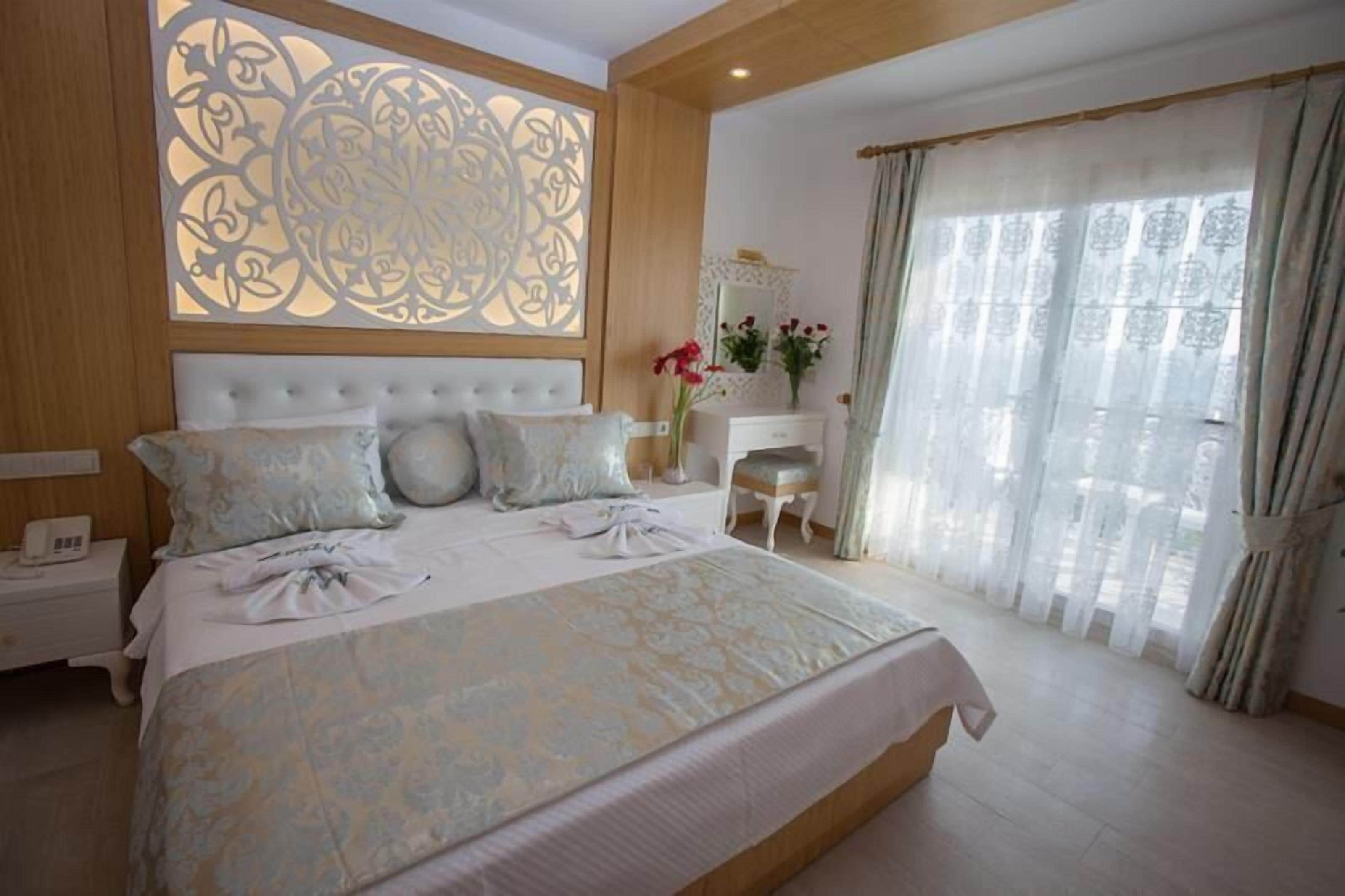 Un dormitorio con una cama grande, una mesita de noche, un aparador y una ventana con cortinas translúcidas.