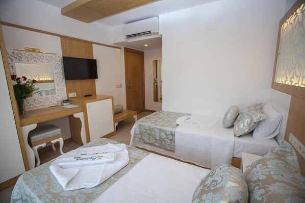 A hotel room with two beds, a desk, a TV, and a shower area. - Hotel Aysima (Kas)