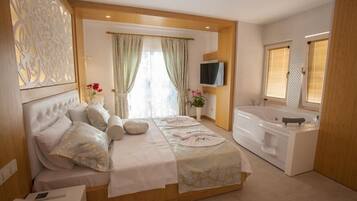 Un dormitorio moderno con una cama grande, una sala de estar separada, una bañera y un televisor.