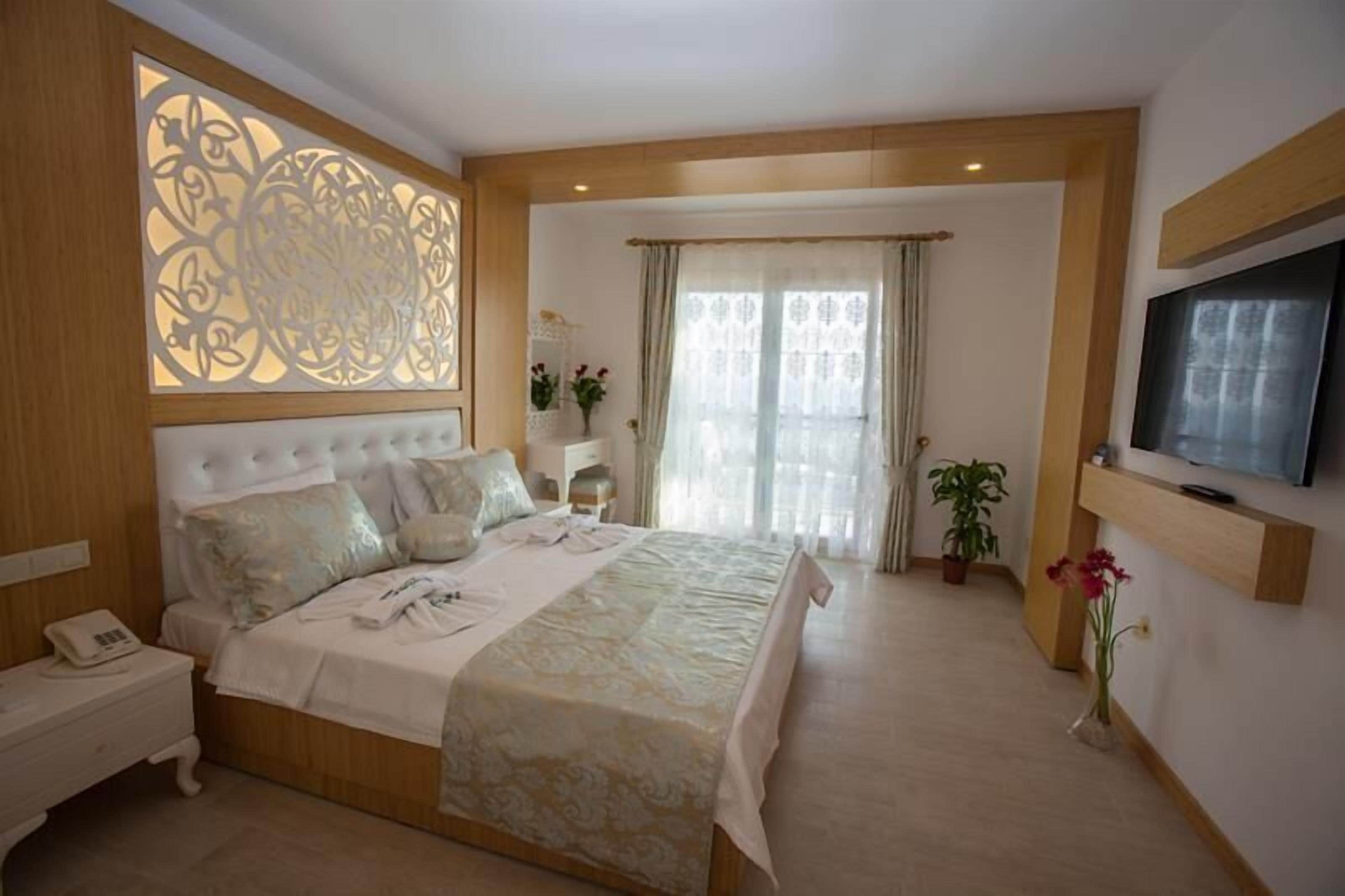 Un dormitorio con una cama grande, una mesita de noche con teléfono, un televisor montado en la pared y un separador decorativo en la pared.